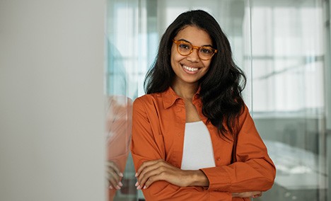 a smiling person with glasses resting against a wall