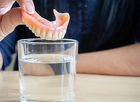 a person putting dentures in a glass of water